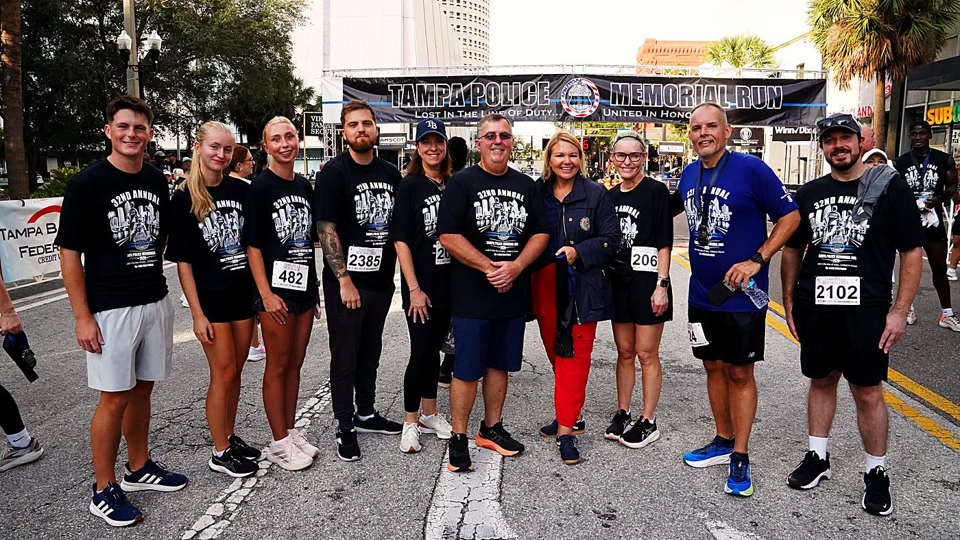 A team of runners in 32nd Annual shirts at the Tampa Police Memorial Run start-line banner