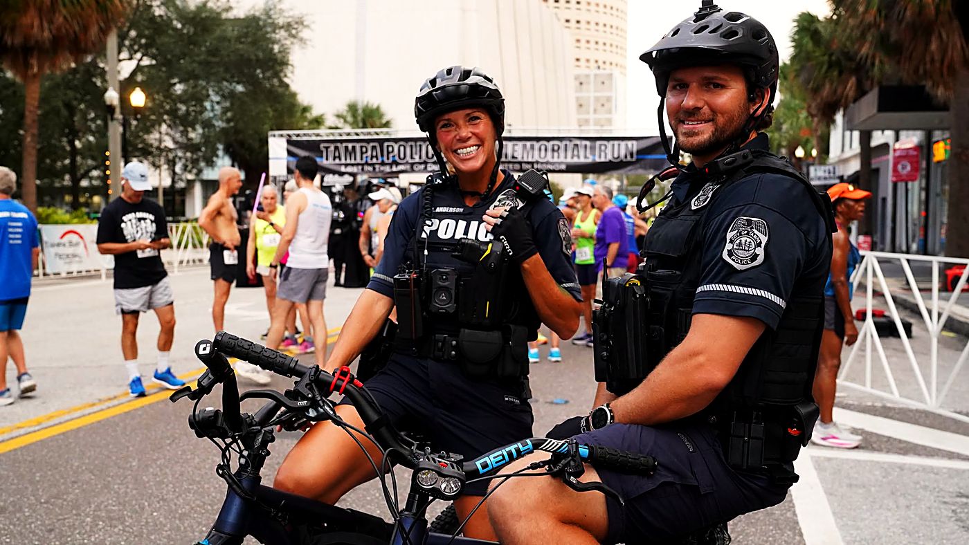 Two Tampa Police bike-patrol officers smiling on their bikes along the race route